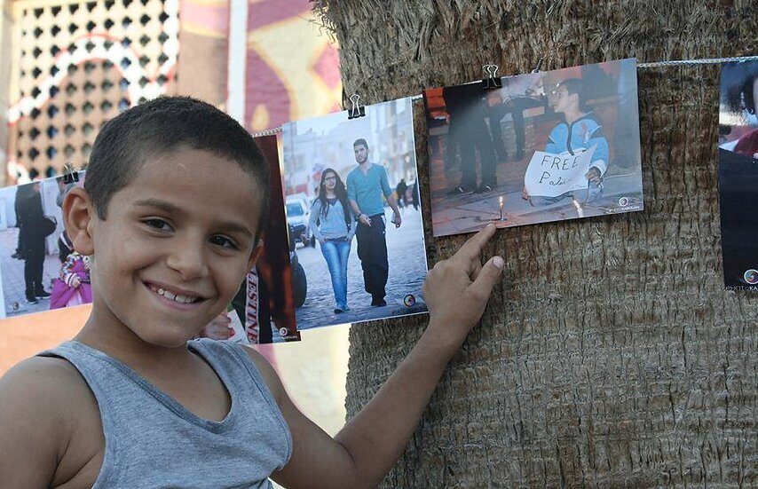 A boy pointing proudly at a photograph in the street exhibition