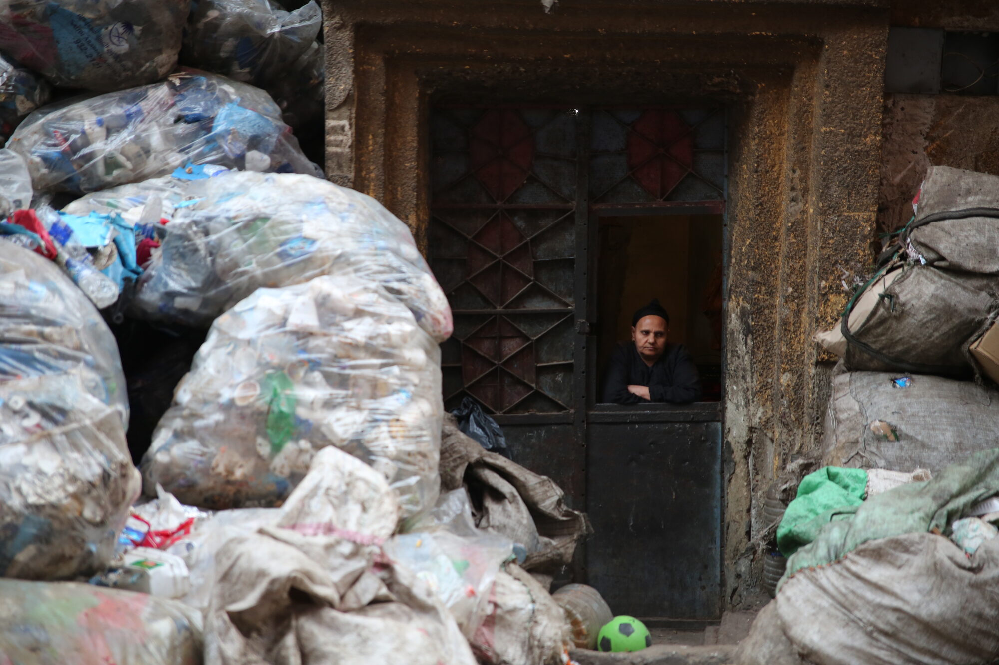 A man looking out from a doorway surrounded by recycling bags