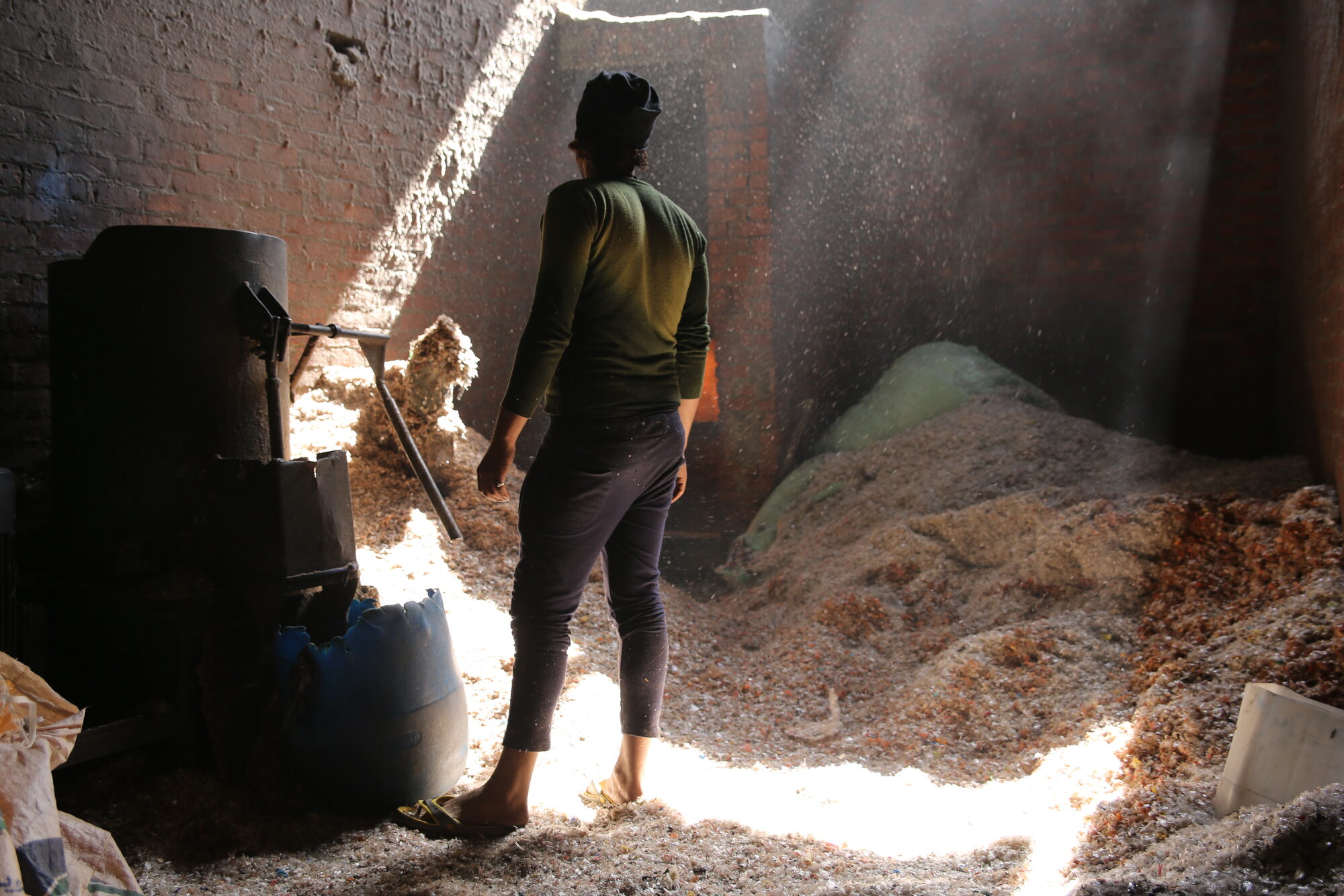 A person standing in a recycling workshop filled with dust and light